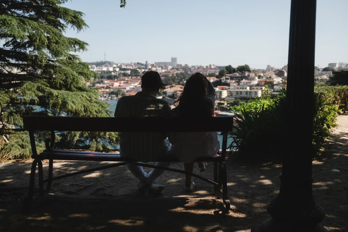 Couple sitting on a shaded park bench overlooking a river and city