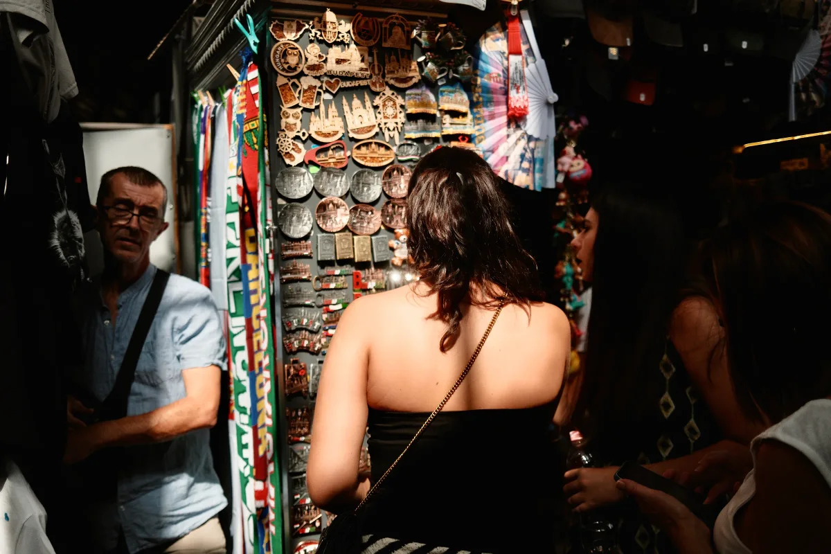 Woman browsing a souvenir stall covered in magnets as a vendor looks on