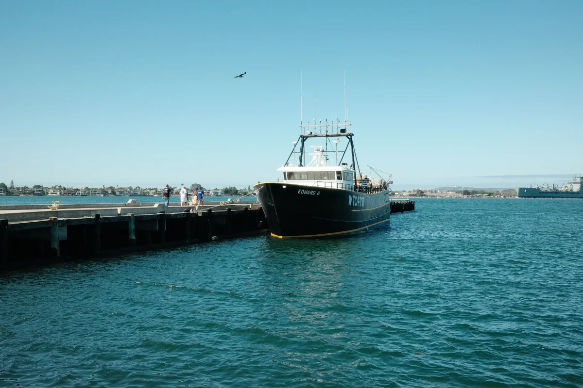 Black fishing trawler moored at a wooden pier on turquoise harbor water under a clear sky
