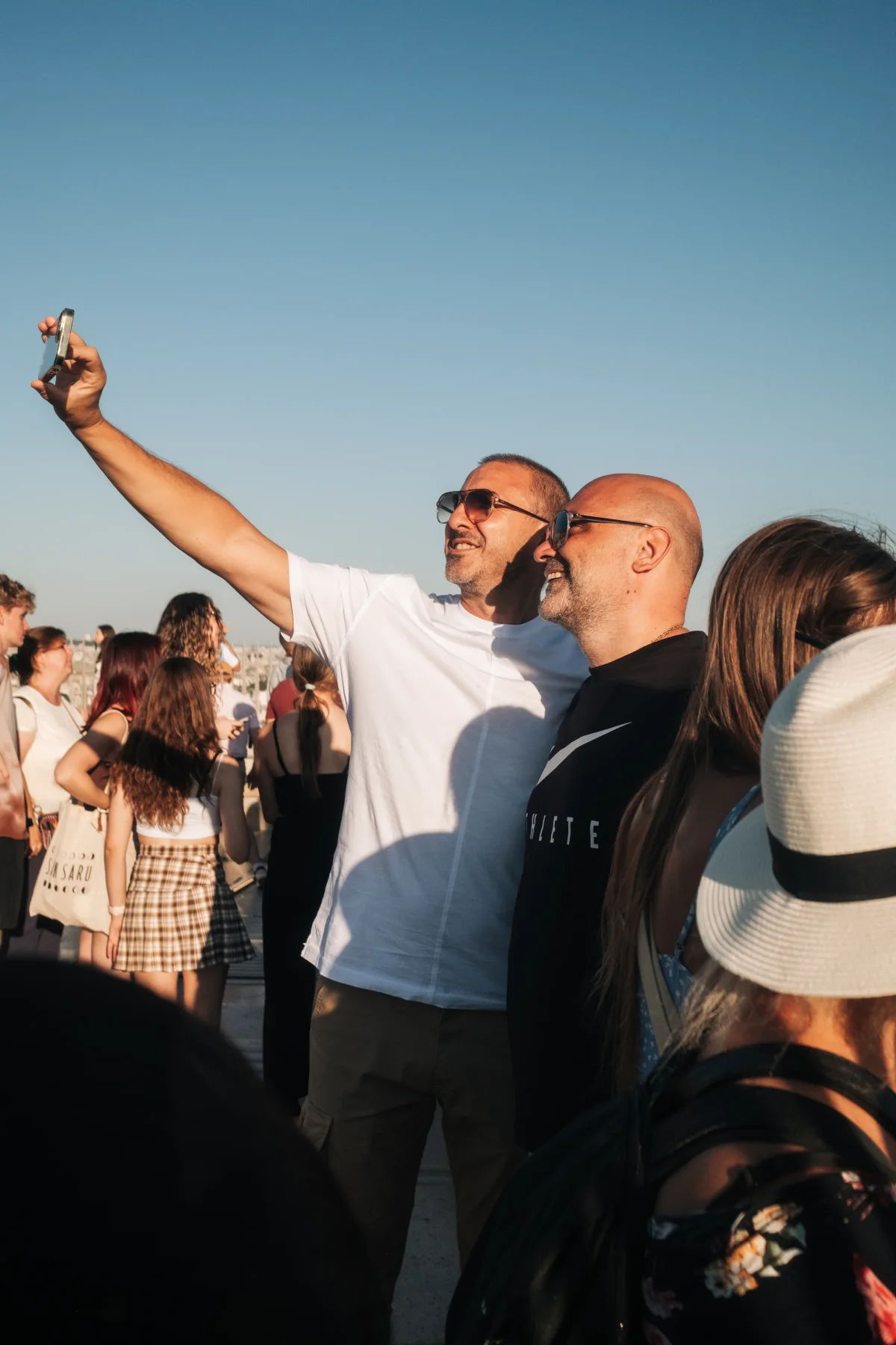 Two men taking a selfie among a crowd of tourists on a sunny terrace