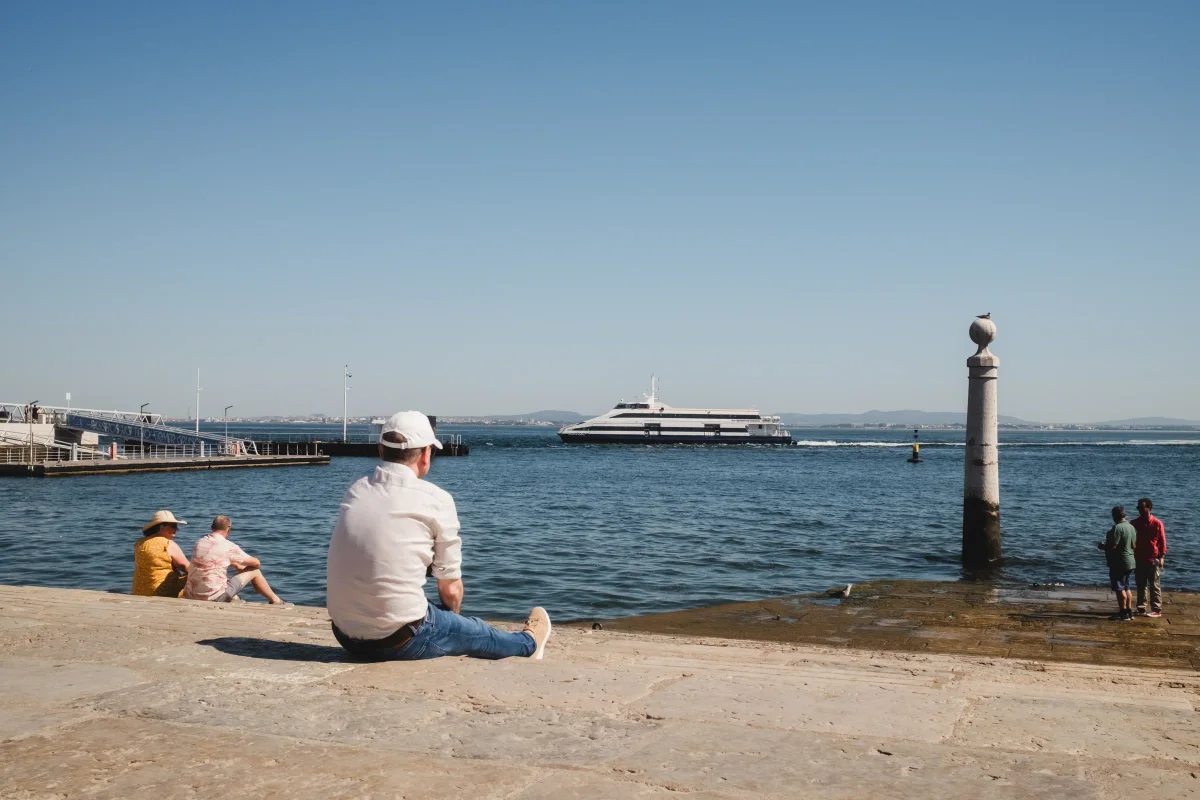 Man sitting on the stone quay beside Cais das Colunas with a ferry on the Tagus
