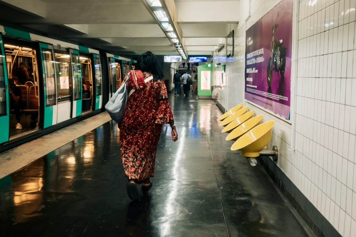 Woman in a red floral dress walking along a Paris Metro platform beside a train