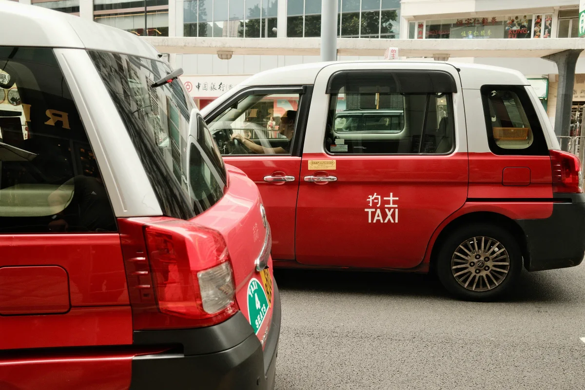 Two red-and-white Hong Kong taxis passing on a city street