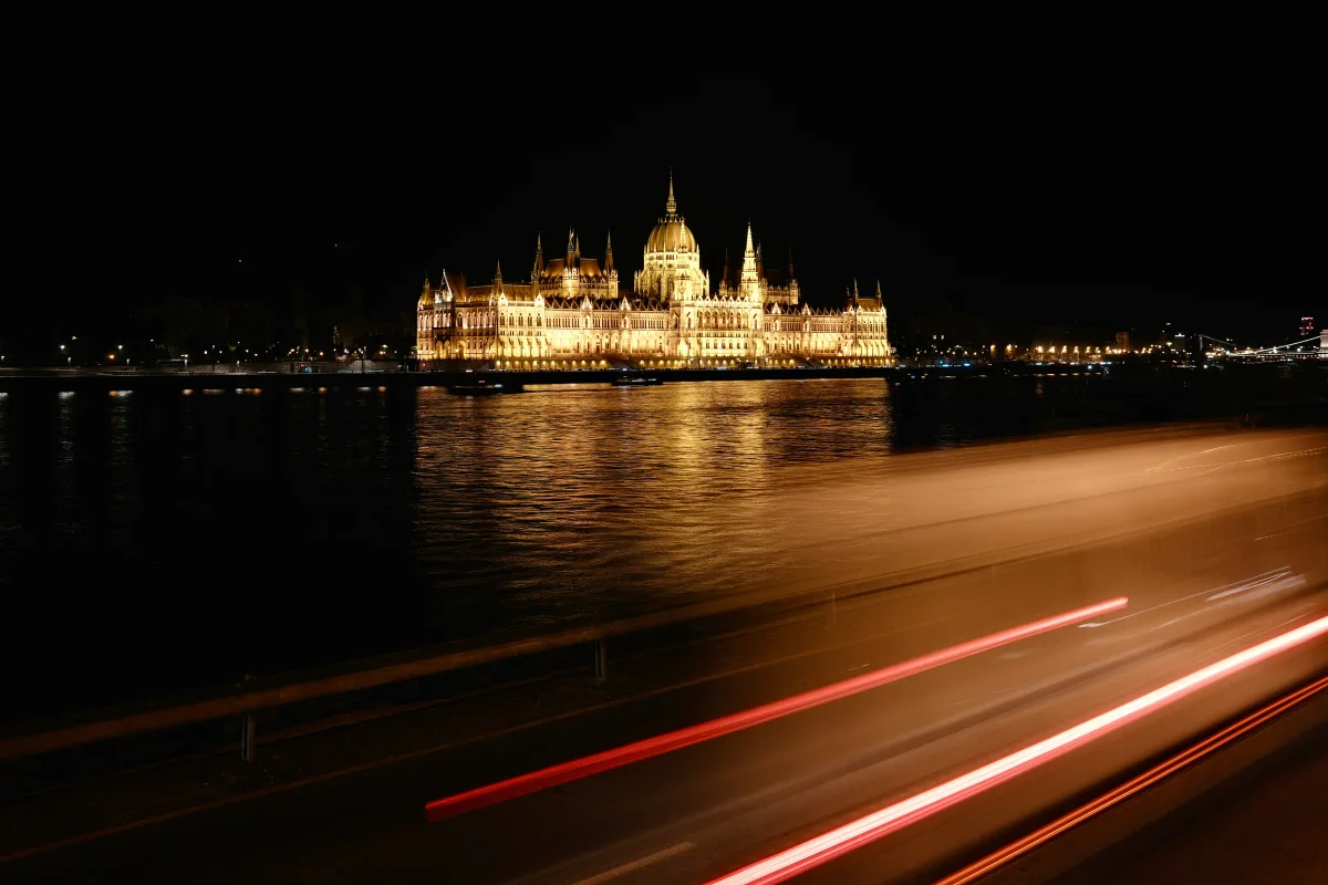 Hungarian Parliament lit gold on the Danube at night with red car light trails
