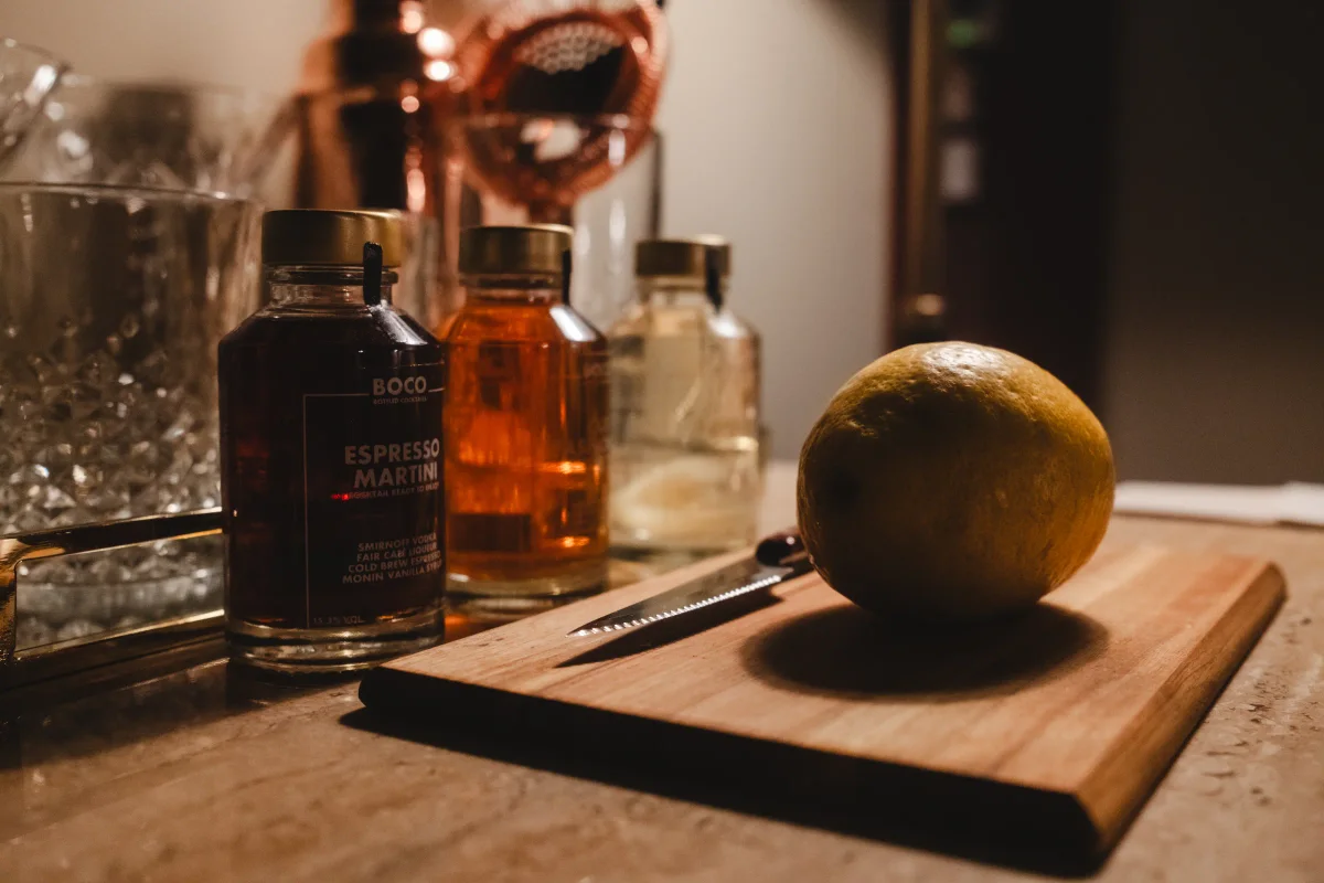 Bar still life of an Espresso Martini bottle, syrups and a lemon on a cutting board
