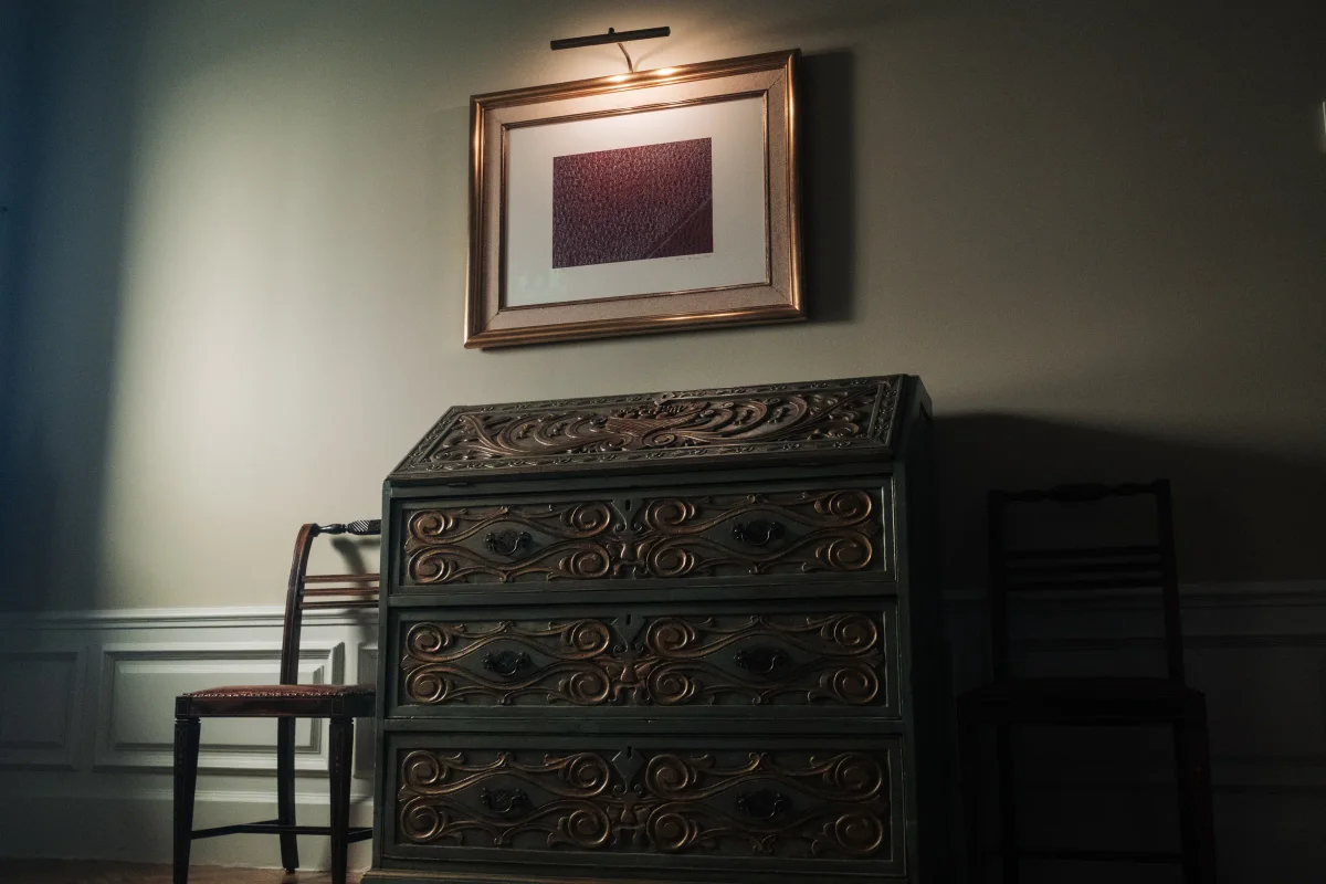 Carved antique writing desk beneath a framed artwork lit by a picture lamp