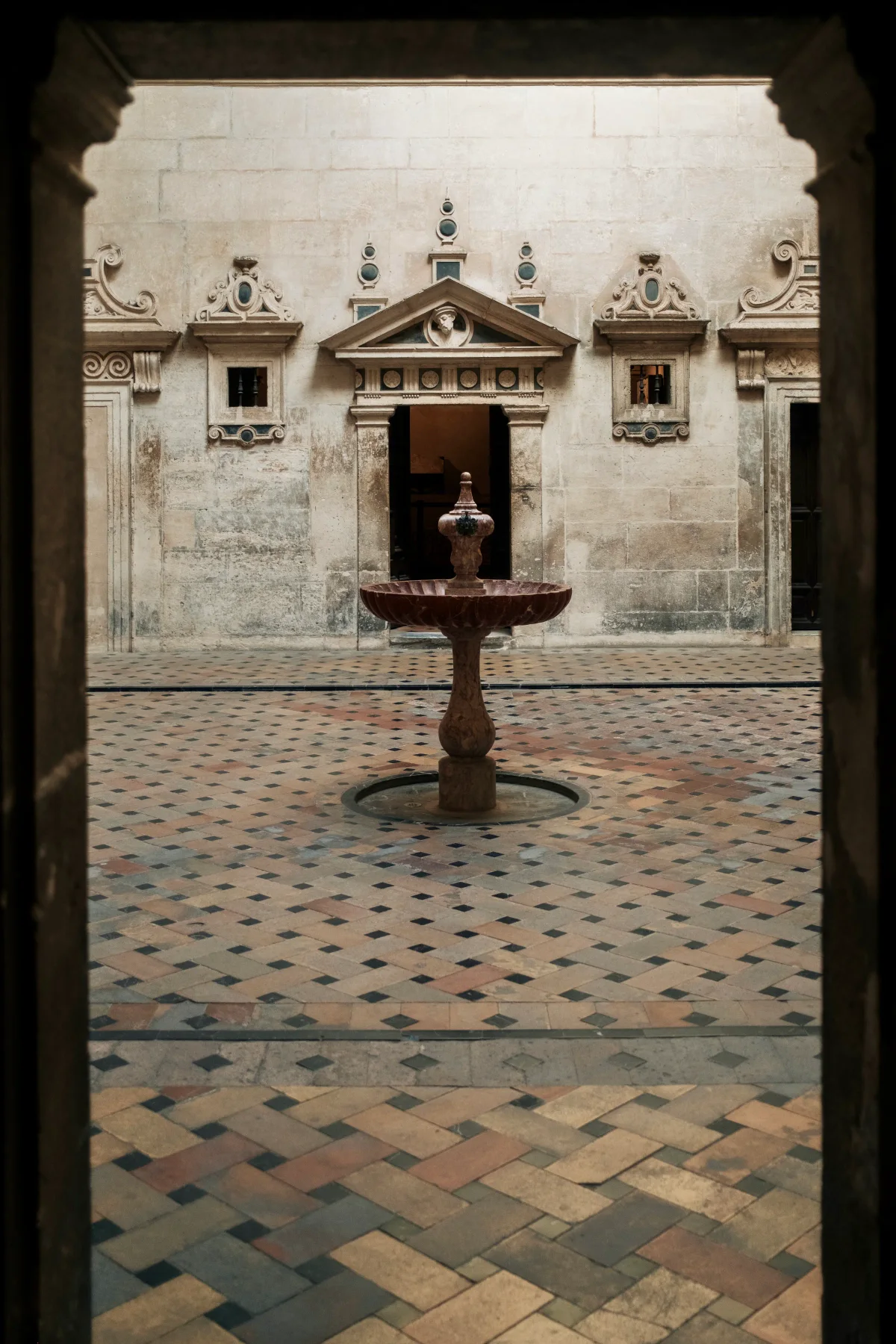 Stone fountain in a tiled courtyard framed by a dark doorway