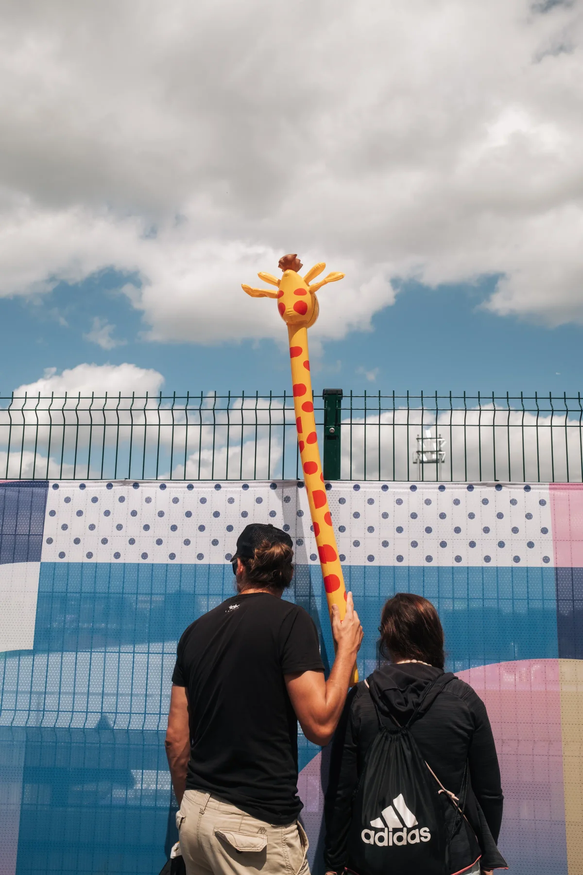 Man holding up an inflatable yellow giraffe beside a woman at a fence