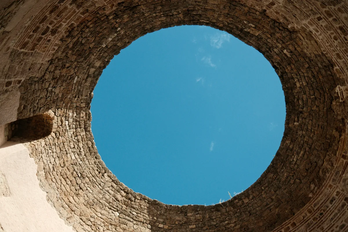 Looking up through a round opening in an ancient brick dome to a blue sky