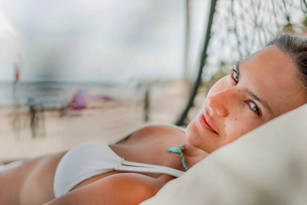 Woman resting on a hammock cushion at the beach, gazing at the camera