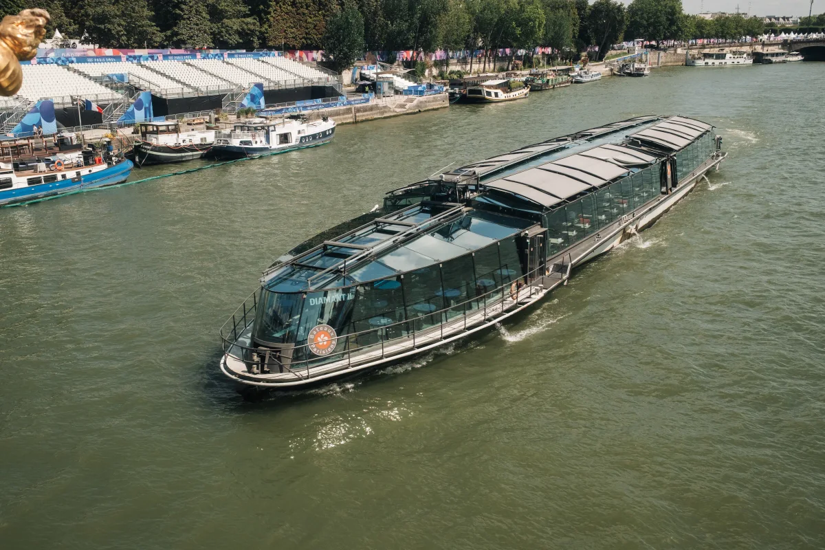 Glass-roofed tour boat cruising the Seine past riverside grandstands