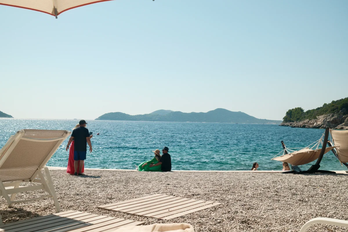 Pebble beach with sun loungers and people facing blue sea and green islands