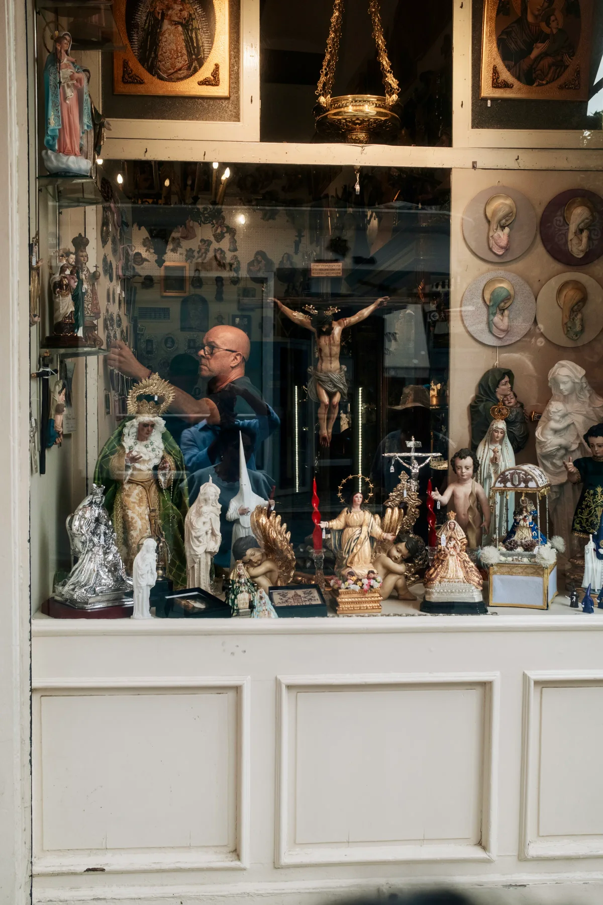 Shop window crowded with religious statues and a shopkeeper arranging them