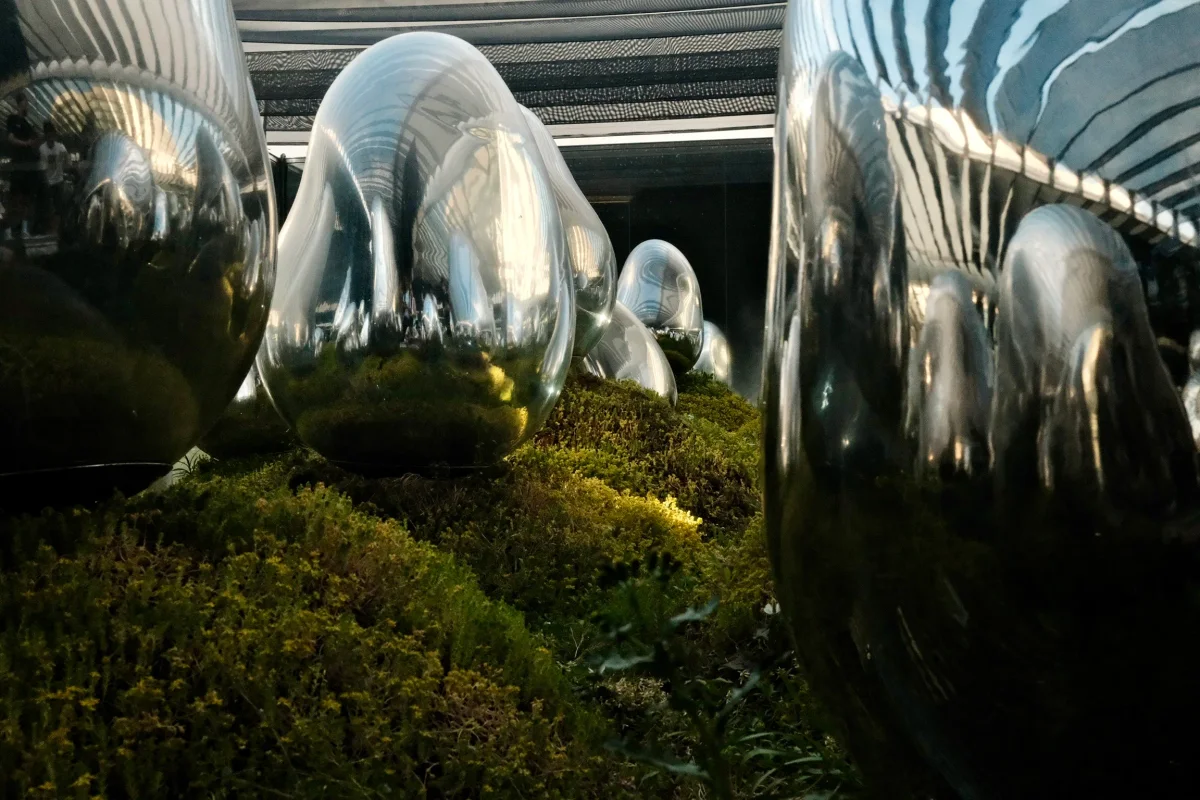 Mirror-polished chrome sculptures rising from a bed of moss and plants