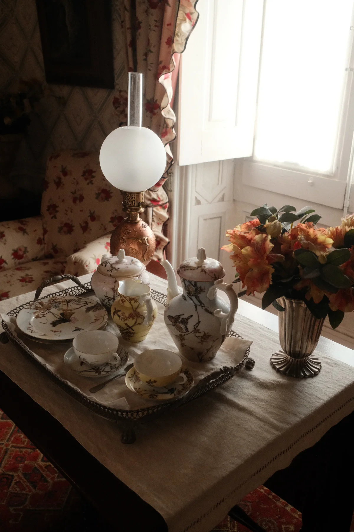 Floral porcelain tea set on a silver tray beside a bright window