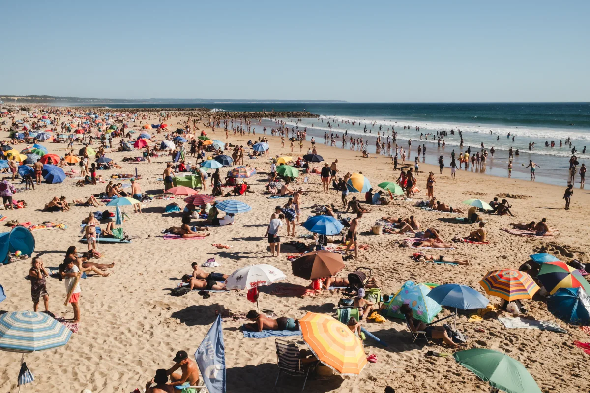 Crowded sandy beach dotted with colorful umbrellas beside the surf