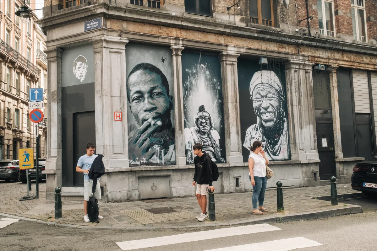 Large black-and-white portrait murals on a corner building with people waiting on the street