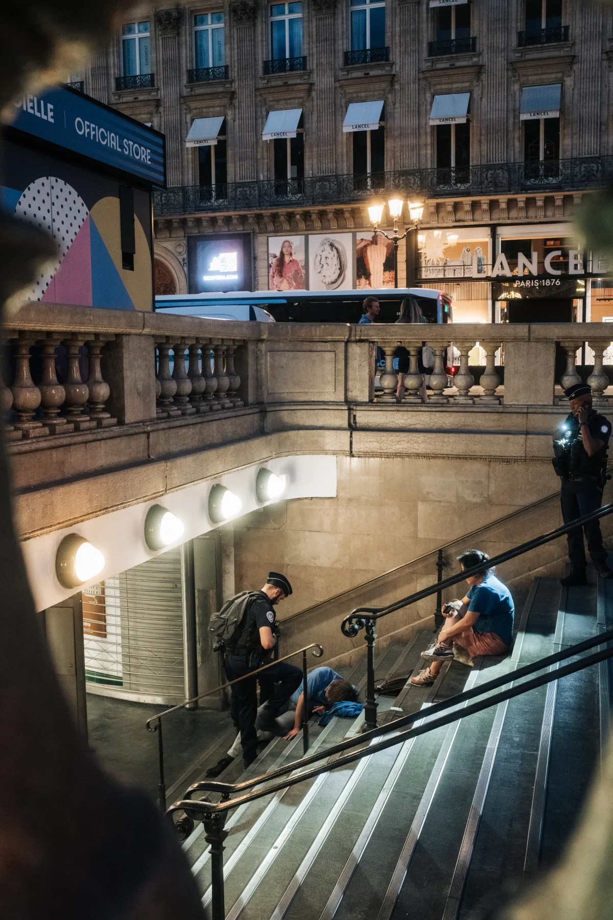 Police officers on Paris Metro stairs at night beneath a lit store sign