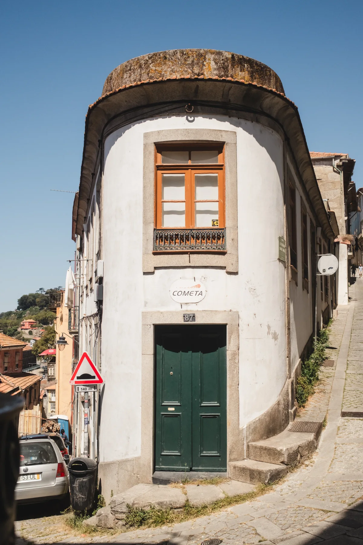 Narrow white corner house with a green door on a steep cobbled street