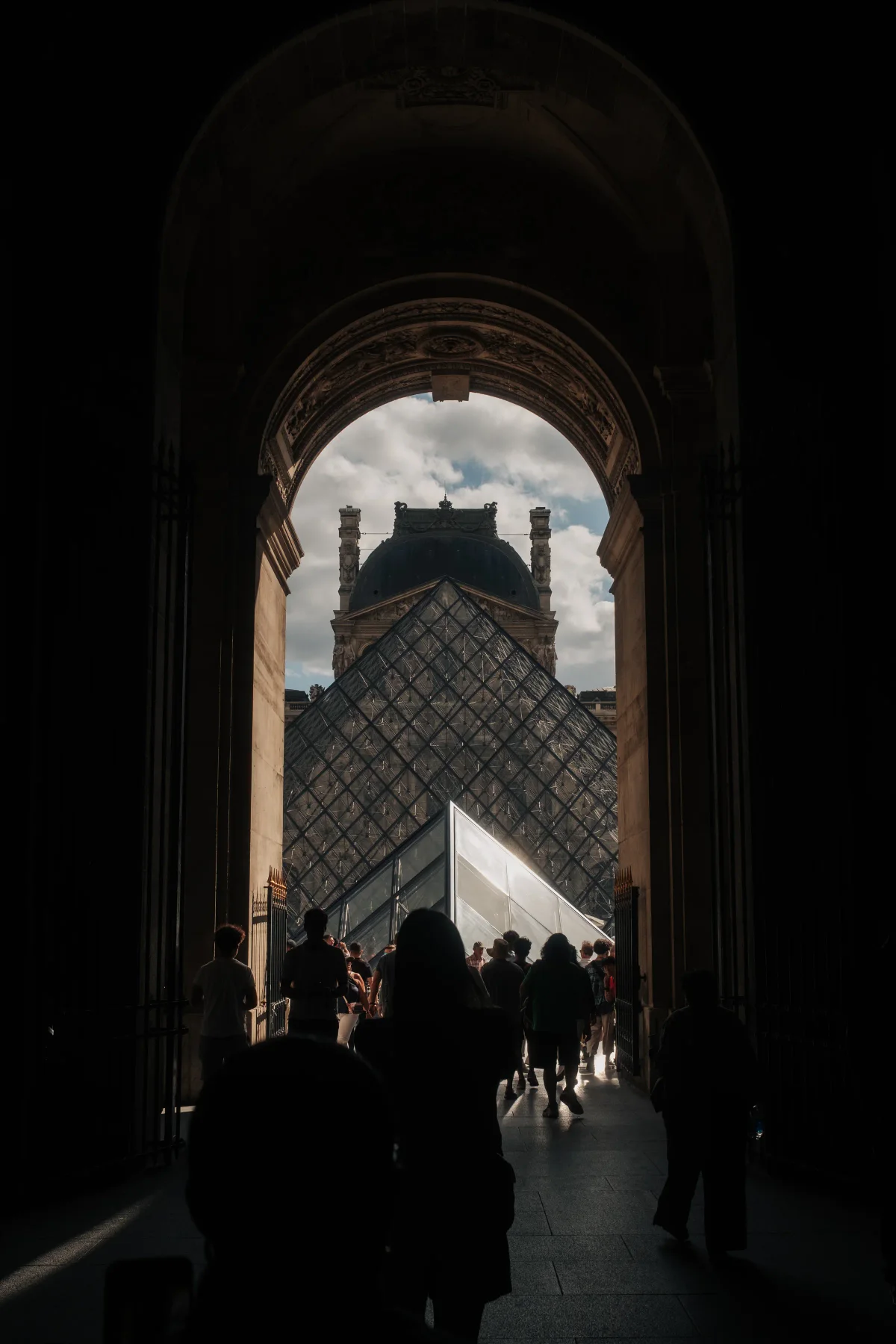 Louvre glass pyramid seen through a dark archway filled with visitors
