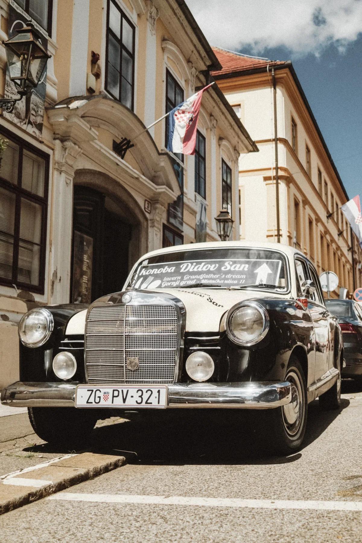 Vintage black Mercedes parked on a Zagreb street beneath a Croatian flag