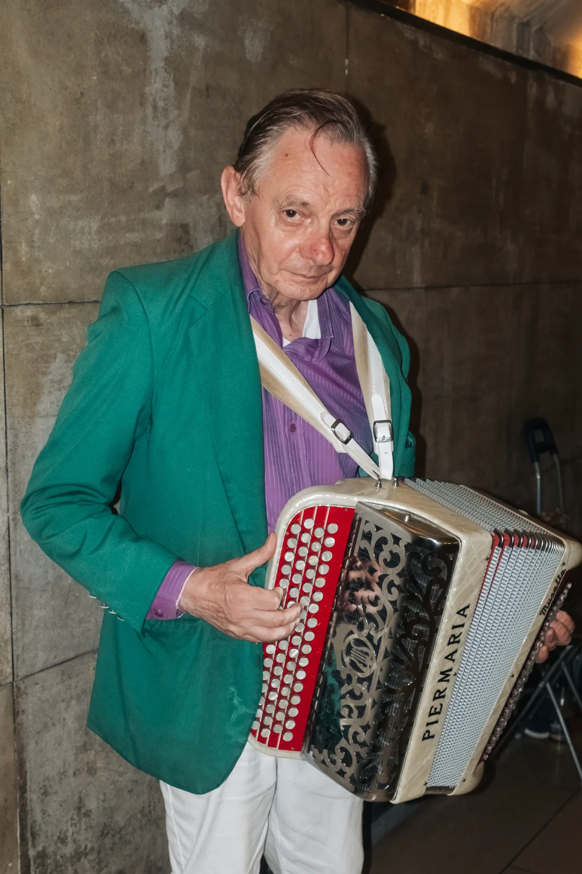 Older accordionist in a green jacket and purple shirt holding his accordion