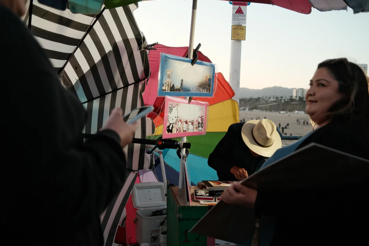 Smiling woman at a colorful vendor stall under striped umbrellas near the beach