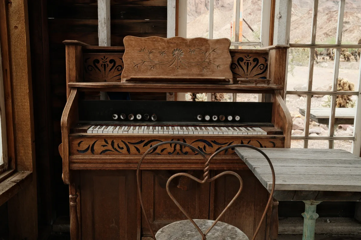 Antique carved pump organ and heart-backed iron chair by a window at Nelson Ghost Town