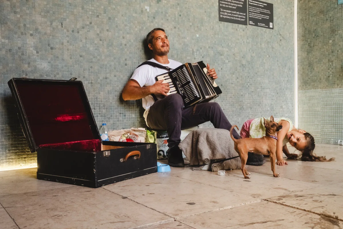 Accordion busker with a small dog and a laughing little girl against a mosaic wall