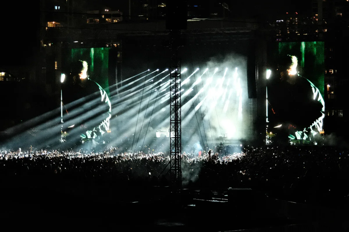 Concert crowd beneath powerful stage light beams and giant video screens at night