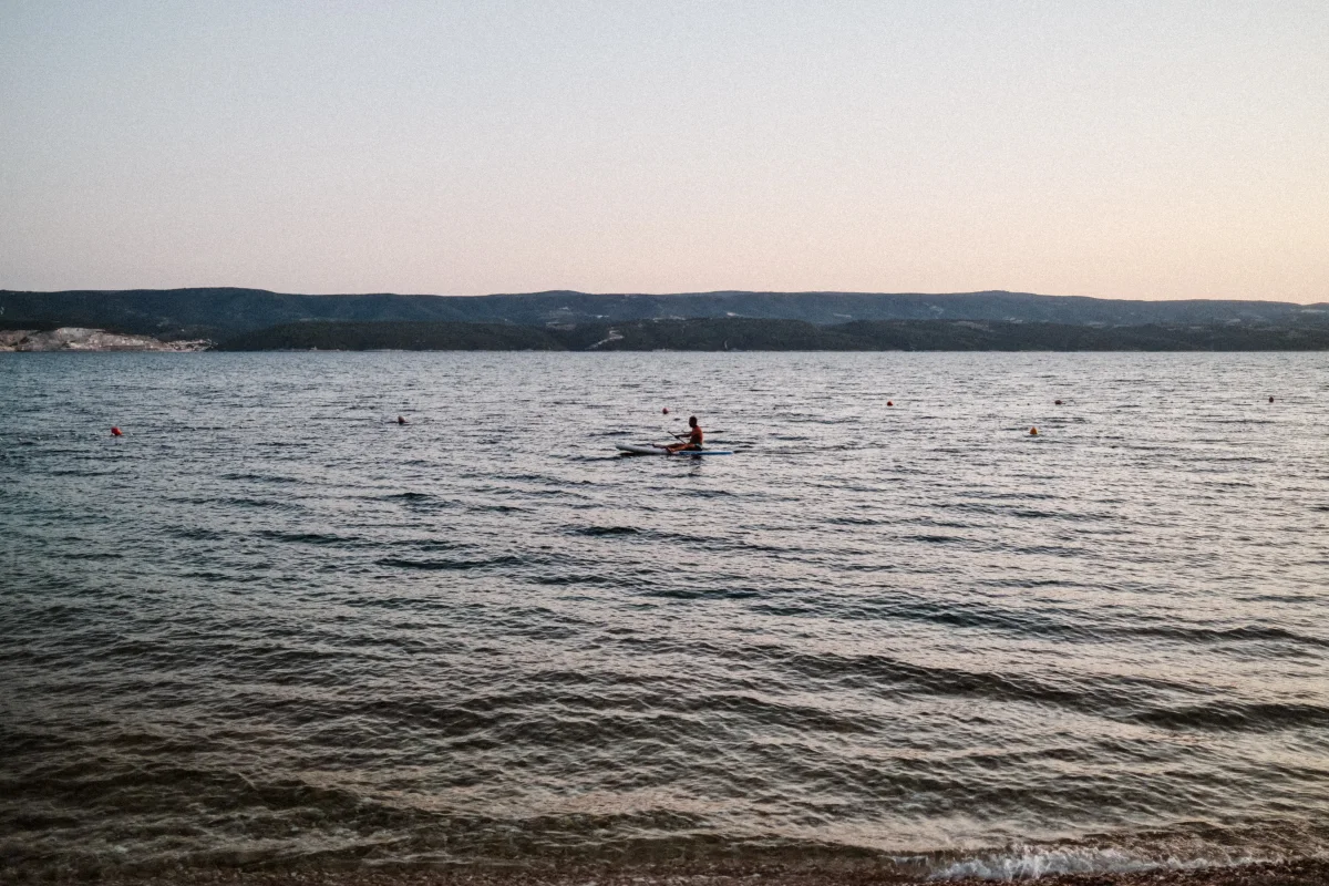 Lone swimmer in calm sea water at dusk with a low coastline behind