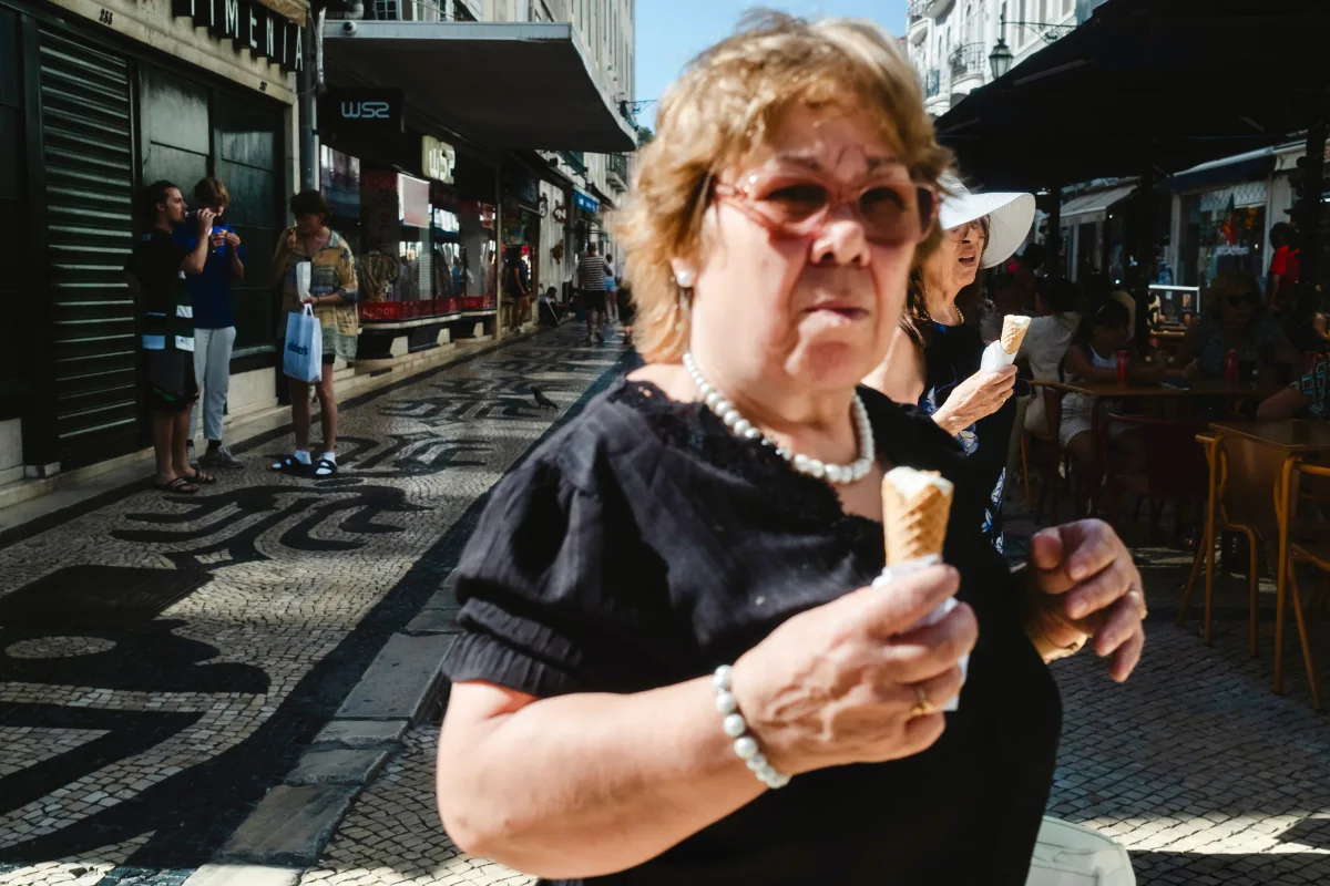 Older woman in sunglasses and pearls eating an ice cream cone on a mosaic sidewalk