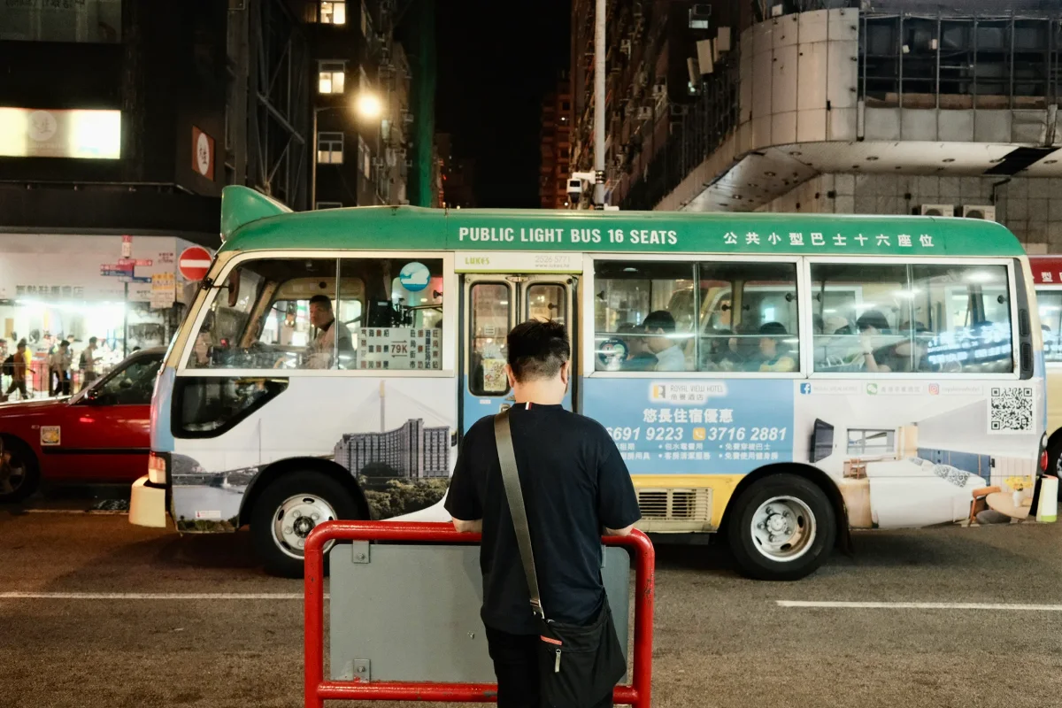 Man waiting beside a green Hong Kong public light bus on a busy street at night