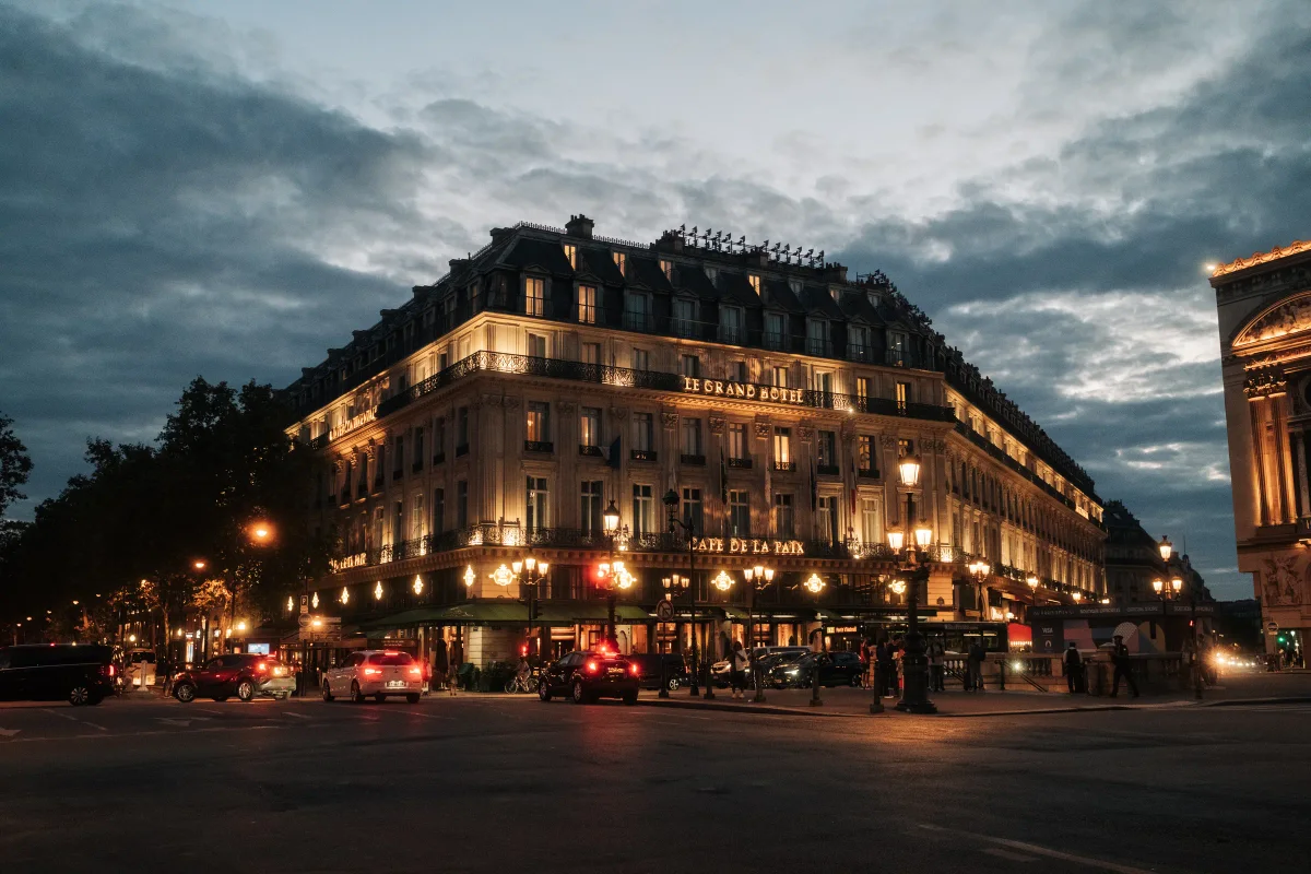 Le Grand Hôtel and Café de la Paix lit at dusk under a cloudy sky in Paris