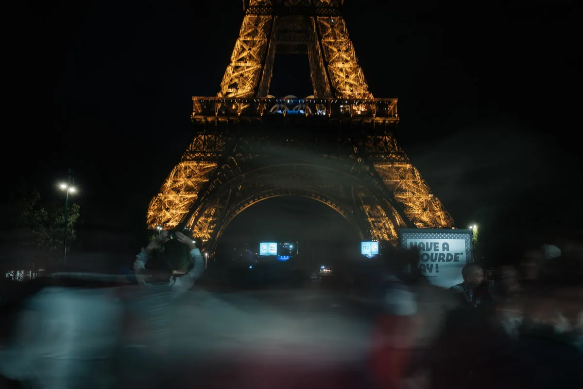 Eiffel Tower lit gold at night above a blurred crowd of passing people