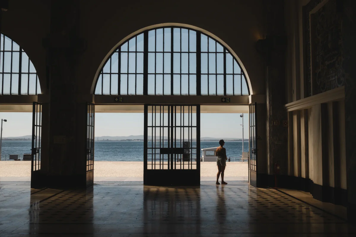 Silhouetted person standing in a grand arched hall facing a bright sunlit waterfront