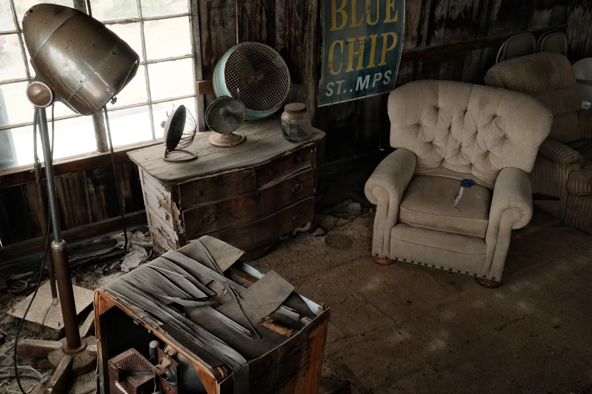 Abandoned room with a tufted armchair, vintage fans and a Blue Chip Stamps sign at Nelson Ghost Town