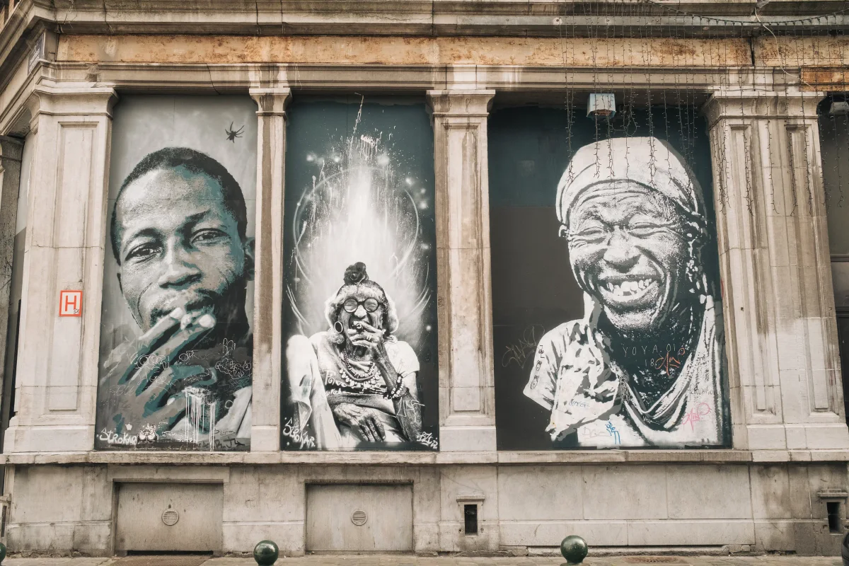 Three large black-and-white portrait murals painted across the windows of an old stone building