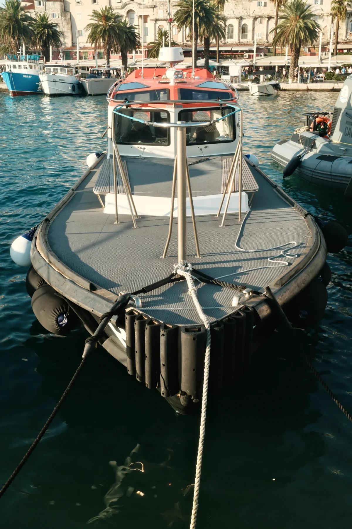 Working boat with black fenders tied at a busy harbor quay