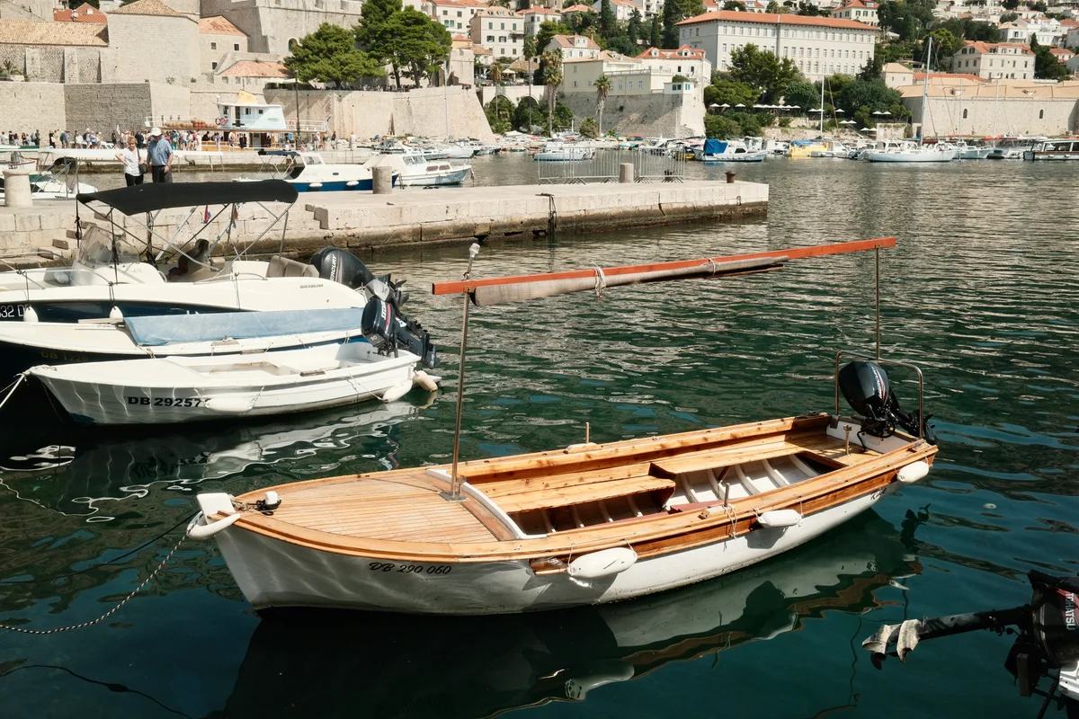 Wooden motor launch floating among small boats in a stone-lined harbor