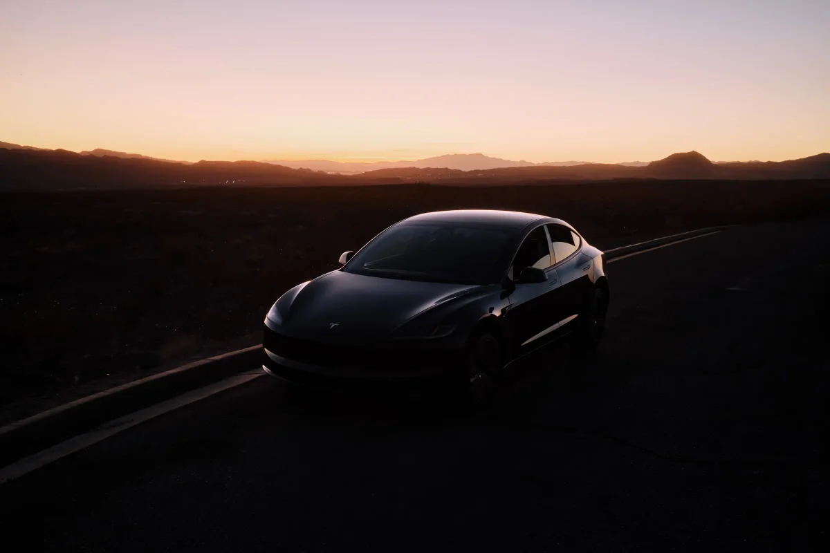 Dark sedan on a desert road silhouetted against mountains and a fading pink sunset
