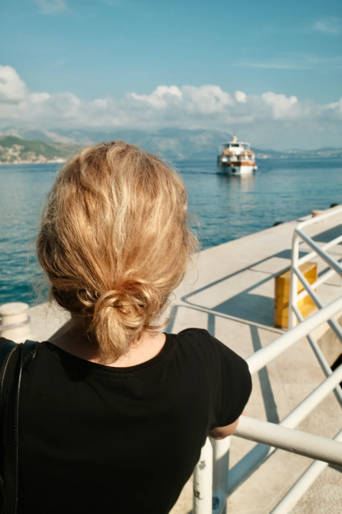A blonde woman waits at the dock for the ferry seen in horizon.