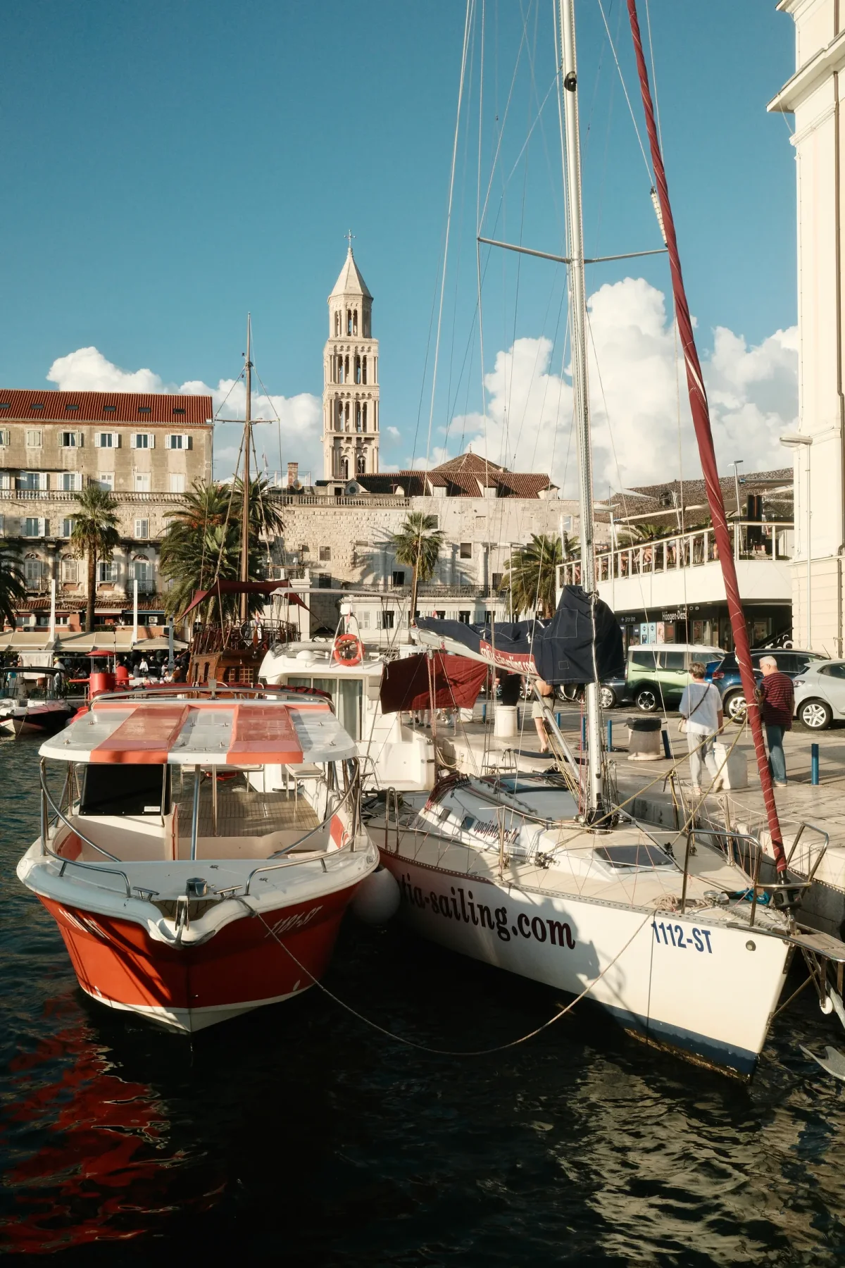 Red passenger boat and sailboat moored below a stone bell tower